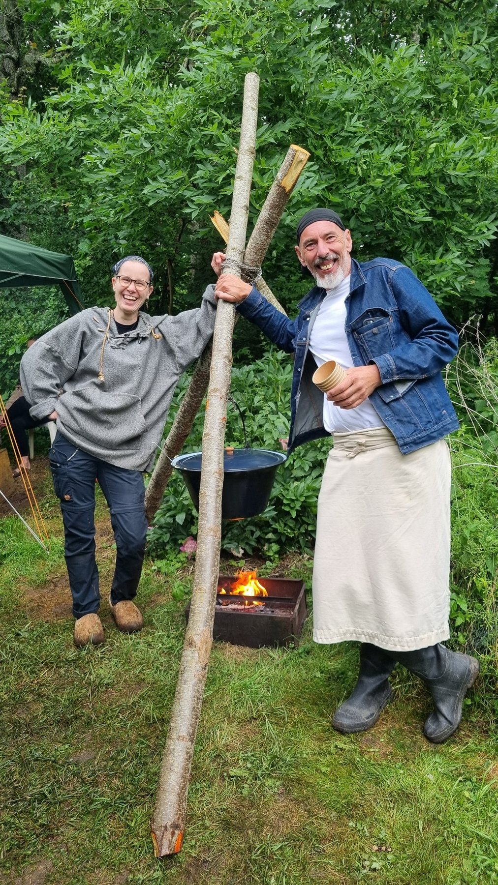 Två glada volontärer lagar mat över öppen eld under Workshop Weekend